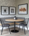 A modern breakfast nook features a light wood round table with a minimalist black metal base, paired with a charcoal grey upholstered bench and two black metal chairs. A subtle geometric peel-and-stick wallpaper adorns the wall, alongside a gallery of abstract art prints. — styling and décor detail