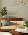 A Mid-Century Modern great room featuring a low-slung sofa in warm beige, a walnut credenza, and a Noguchi coffee table. Accents of sage green and a muted sky blue are visible in throw pillows and a ceramic vase, with a Sputnik chandelier overhead and a Fiddle Leaf Fig in a white planter. — alternate angle