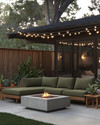 A cozy Mid-Century Modern backyard featuring a low-profile sectional with olive green cushions, a sleek concrete fire pit, and warm string lights draped overhead, complemented by teak side tables and potted snake plants. — alternate angle