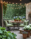 A cozy traditional patio featuring a wrought iron dining set with sage green cushions, a wooden dining table, and warm string lights draped overhead. Terracotta pots filled with lush greenery and blooming hydrangeas are placed around a stone fire pit. — styling and décor detail