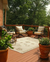 A traditional deck featuring warm-toned cedar decking and railings, wrought iron furniture with cream cushions, an outdoor rug in a natural beige, and terracotta planters filled with green foliage, all under soft, natural light. — styling and décor detail