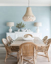 A coastal dining room featuring a light oak modern dining table, vintage rattan chairs, a distressed white buffet, and a contemporary capiz shell chandelier, with walls painted in a soft Palladian Blue. — close-up of textures and materials