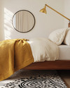 A renter-friendly Mid-Century Modern bedroom featuring a walnut platform bed with a cream duvet, a mustard yellow knit throw, and a graphic black and white area rug. Brass multi-arm floor lamp and a simple round mirror accent the space. — close-up of textures and materials
