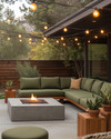 A cozy Mid-Century Modern backyard featuring a low-profile sectional with olive green cushions, a sleek concrete fire pit, and warm string lights draped overhead, complemented by teak side tables and potted snake plants.