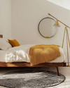 A renter-friendly Mid-Century Modern bedroom featuring a walnut platform bed with a cream duvet, a mustard yellow knit throw, and a graphic black and white area rug. Brass multi-arm floor lamp and a simple round mirror accent the space. — styling and décor detail