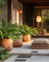 A serene Japandi-style driveway featuring large unglazed terracotta planters with lush green ferns, smooth concrete stepping stones, and subtle solar-powered pathway lights casting a warm glow. A simple wooden bench with a woven cushion sits near the entrance, embodying natural textures and minimalist design. — close-up of textures and materials