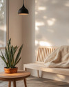A Scandinavian porch featuring a light ash slatted bench with a cream knit throw, a small round teak coffee table, and a sculptural snake plant in a terracotta pot, all under the soft glow of a matte black outdoor pendant light. — alternate angle
