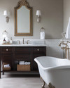 Traditional bathroom featuring a white clawfoot tub, a dark wood console vanity with a Carrara marble top, polished nickel fixtures, and an ornate gilded mirror above the sink, all under warm sconce lighting. — styling and décor detail