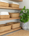 Cozy boho laundry room featuring light oak floating shelves, natural rattan laundry baskets, a woven jute rug, and a ceramic planter with a lush Pothos plant, all under soft, warm lighting. — close-up of textures and materials
