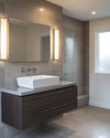 Modern bathroom with a floating dark wood vanity, white vessel sink, and large format grey wall tiles. Integrated LED mirror lighting and recessed ceiling lights illuminate the space, complemented by polished chrome fixtures.