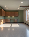 Clean Mid-Century Modern garage featuring walnut flat-panel cabinetry, a polished light grey epoxy floor, recessed LED lighting, and a subtle sage green accent wall behind a minimalist workbench. — close-up of textures and materials