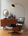 A sophisticated Mid-Century Modern library featuring an Eames Lounge Chair in black leather and walnut, an Arco floor lamp arching over, and a teak credenza displaying abstract ceramic vases and a vintage globe, all under the warm glow of a Sputnik chandelier. — close-up of textures and materials