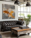 An industrial landscape living room featuring a charcoal distressed leather Chesterfield sofa, a reclaimed wood coffee table on caster wheels, and a large abstract painting in grey and burnt sienna tones, under exposed metal pendant lighting. — close-up of textures and materials