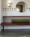 A Mid-Century Modern mudroom featuring a walnut slatted bench, polished concrete flooring, and an olive green upholstered cushion. Brass hooks line the wall above, with a circular mirror and a small white globe sconce adding modern accents. — styling and décor detail