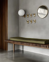 A Mid-Century Modern mudroom featuring a walnut slatted bench, polished concrete flooring, and an olive green upholstered cushion. Brass hooks line the wall above, with a circular mirror and a small white globe sconce adding modern accents. — close-up of textures and materials