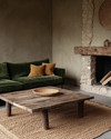 A Rustic Landscape living room featuring a deep forest green velvet sofa, a reclaimed wood coffee table, and a rough-hewn stone fireplace. Natural light illuminates the warm greige walls, complemented by woven jute rugs and subtle ochre throw pillows. — close-up of textures and materials