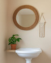 A cozy boho powder room featuring a round rattan mirror above a white pedestal sink, a small Pothos plant in a terracotta pot, and a macrame wall hanging on a light beige wall. — styling and décor detail