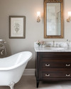 Traditional bathroom featuring a white clawfoot tub, a dark wood console vanity with a Carrara marble top, polished nickel fixtures, and an ornate gilded mirror above the sink, all under warm sconce lighting. — close-up of textures and materials