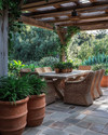 A rustic patio featuring a large flagstone patio surface, a solid wood dining table with woven rattan chairs, and terracotta planters filled with lush green plants under a natural wood pergola. — close-up of textures and materials