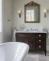 Traditional bathroom featuring a white clawfoot tub, a dark wood console vanity with a Carrara marble top, polished nickel fixtures, and an ornate gilded mirror above the sink, all under warm sconce lighting. — alternate angle