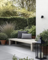 A Scandinavian backyard featuring a light grey wooden deck, a simple slatted teak bench with a charcoal grey outdoor cushion, and a minimalist black metal lantern. Greenery includes potted evergreen shrubs and ornamental grasses in terracotta pots, creating a serene, natural ambiance. — close-up of textures and materials