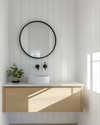 A bright Scandinavian powder room with white walls, a light wood floating vanity, a minimalist round mirror, and a single black wall-mounted faucet, accented by a small green plant. — close-up of textures and materials