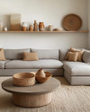 A Modern Craft living room with a large, comfortable sectional sofa in a warm grey performance fabric, an oak coffee table with a matte finish, and a woven jute rug. Walls are painted in a soft off-white, complemented by shelves displaying hand-thrown ceramic vases and a large woven basket for storage. — styling and décor detail
