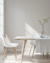 A bright Scandinavian dining room featuring a light birch wood dining table, minimalist white chairs, a simple linen tablecloth, and a clear glass vase with a single green branch, all set against soft grey walls. — alternate angle