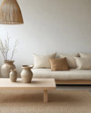 A serene Japandi living room featuring a low-slung sofa in natural linen, a simple light oak coffee table, and a woven jute rug, complemented by a bamboo pendant light and ceramic vases in muted tones. — styling and décor detail