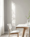 A bright Scandinavian dining room featuring a light birch wood dining table, minimalist white chairs, a simple linen tablecloth, and a clear glass vase with a single green branch, all set against soft grey walls. — close-up of textures and materials