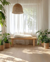 A bright Scandinavian sunroom featuring light oak flooring, a minimalist birch wood bench, and a rattan pendant light. Natural linen curtains filter the sunlight, while a faux sheepskin throw and various green plants in unglazed ceramic pots add texture and life. — close-up of textures and materials
