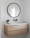 A bright Scandinavian powder room with white walls, a light wood floating vanity, a minimalist round mirror, and a single black wall-mounted faucet, accented by a small green plant. — styling and décor detail