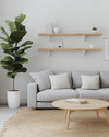 A bright Scandinavian family room featuring a light grey sofa with linen cushions, a round blonde wood coffee table, and a large jute rug. Walls are painted in a soft off-white, complemented by a tall fiddle leaf fig plant in a white pot, and minimalist floating shelves. — styling and décor detail