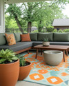 A family-friendly Mid-Century Modern patio featuring a low-profile charcoal grey L-shaped sectional with olive green performance fabric cushions, a geometric outdoor rug in burnt orange and teal, and teak wood accent tables. Large, sculptural ceramic planters with pet-safe plants are arranged around the seating area, with a subtle concrete water bowl for pets integrated into the design. — close-up of textures and materials