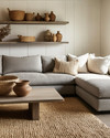 A Modern Craft living room with a large, comfortable sectional sofa in a warm grey performance fabric, an oak coffee table with a matte finish, and a woven jute rug. Walls are painted in a soft off-white, complemented by shelves displaying hand-thrown ceramic vases and a large woven basket for storage. — close-up of textures and materials