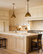 A cozy traditional kitchen featuring creamy off-white shaker cabinets, a large oak island with a honed marble top, brushed brass hardware, and a bridge faucet, illuminated by layered lighting. — view 4