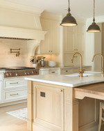 A cozy traditional kitchen featuring creamy off-white shaker cabinets, a large oak island with a honed marble top, brushed brass hardware, and a bridge faucet, illuminated by layered lighting. — view 3
