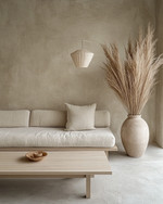 A minimalist Japandi living room featuring a low-profile sofa in natural linen, a light ash wood coffee table, and a large, unglazed ceramic vase with dried pampas grass. The walls are painted in a warm grey, complemented by soft, diffused light from a paper-shade floor lamp. — view 2