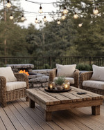 Rustic deck featuring reclaimed wood decking, a rough-hewn teak coffee table, and woven rattan armchairs with natural linen cushions. Edison bulb string lights are draped overhead, casting a warm glow, complemented by a stone fire pit in the background. — view 4