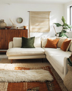 A bohemian great room blending vintage and modern elements, featuring a cream sectional sofa, a mid-century teak credenza, layered jute and sheepskin rugs, and a mix of terracotta and sage green accents.