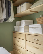 A Japandi-style closet featuring light ash wood shelving and drawers, cream linen storage boxes, and a subtle sage green accent wall, bathed in soft, natural light. — view 3