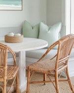 A serene coastal breakfast nook featuring a round bleached oak table with two woven rattan chairs and a light grey upholstered bench, accented with pale seafoam green throw pillows and a natural jute rug. — close-up of textures and materials