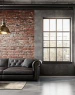 An industrial living room with a cohesive color story featuring a charcoal leather sofa, exposed brick wall, and a large metal-framed window. Warm grey walls, a polished concrete floor, and an aged brass pendant light add to the calm, urban aesthetic. — styling and décor detail