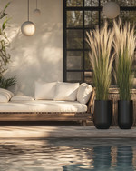 A Scandinavian poolside area featuring a large reclaimed teak daybed with cream linen cushions, oversized woven rattan armchairs, and matte black metal planters with tall Horsetail Reed plants, all under the soft glow of spherical outdoor lanterns. — alternate angle