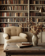 Farmhouse library with a large built-in bookshelf filled with books, a comfortable armchair upholstered in a warm beige fabric, and a weathered wood coffee table adorned with a vase of dried flowers, all under the soft glow of a bronze-finished floor lamp. — styling and décor detail