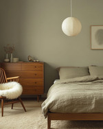 A Japandi bedroom blending vintage and modern, featuring a low oak bed, a mid-century modern teak dresser, a modern rice paper pendant light, and a vintage spindle-back chair with a sheepskin throw, all in muted tones of soft grey, beige, and sage green. — styling and décor detail