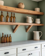 Calm farmhouse home bar featuring warm white shaker cabinets, a honed light grey soapstone countertop, and open reclaimed wood shelving. Amber glass bottles, ceramic pitchers, and matte black hardware complement the serene sage green accent wall. — close-up of textures and materials