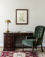 A traditional small home office featuring a dark wood secretary desk with a brass lamp, a comfortable upholstered desk chair in deep green, and a classic Persian rug in muted red and cream tones. A framed botanical print hangs on the wall. — close-up of textures and materials