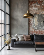 An industrial living room with a cohesive color story featuring a charcoal leather sofa, exposed brick wall, and a large metal-framed window. Warm grey walls, a polished concrete floor, and an aged brass pendant light add to the calm, urban aesthetic. — alternate angle