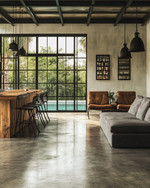 Industrial poolhouse interior featuring polished concrete floors, a reclaimed wood bar, and black steel framed windows looking out to a pool. A charcoal linen sofa, vintage leather armchairs, and matte black industrial pendant lights create a vintage-modern fusion. — alternate angle
